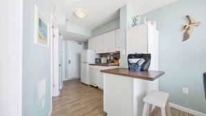 Une cuisine compacte avec des meubles blancs, un plan de travail en bois et un petit tabouret blanc.