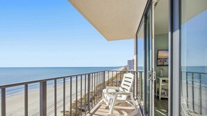Un balcon avec vue sur la plage, une porte vitrée et un petit coin salon avec des chaises.