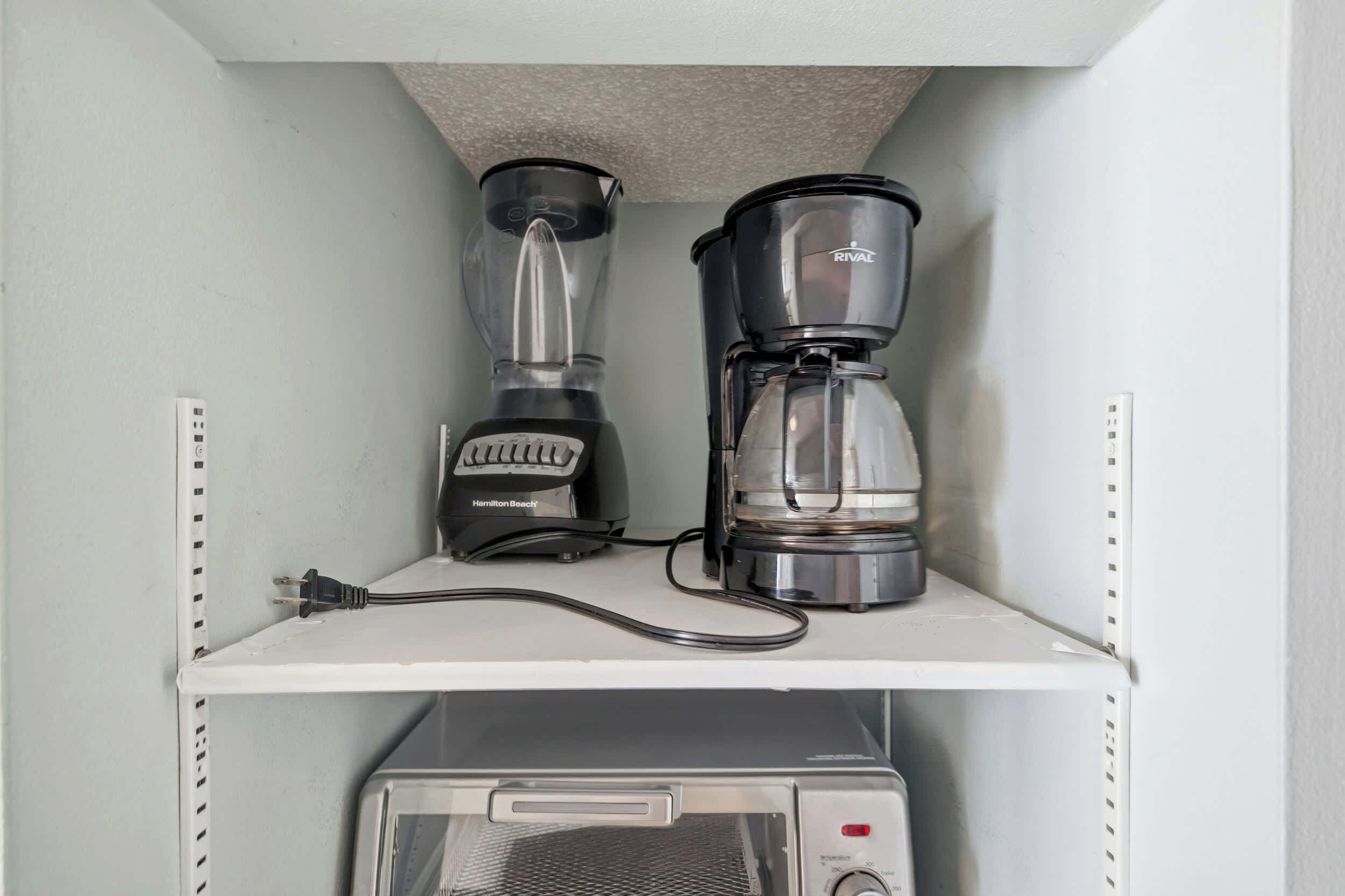 A kitchenette with a Hamilton Beach blender and a Rival coffee maker on a white shelf, and a microwave below.