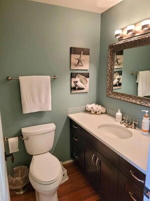 Une salle de bain avec des toilettes, un lavabo et des meubles sombres. Des serviettes sont suspendues sur un porte-serviettes et un miroir est placé au-dessus du lavabo.
