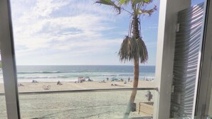 Vista a la playa desde una habitación con una mesa de vidrio y sillas blancas.