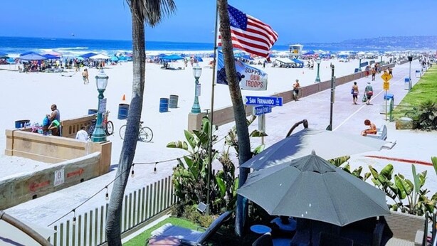Un patio frente a la playa con mobiliario exterior, una palmera y una bandera estadounidense.