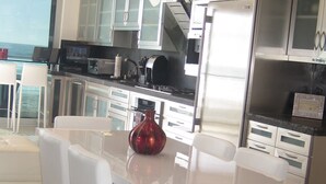 Una cocina moderna con armarios blancos, electrodomésticos de acero inoxidable y una mesa de comedor de vidrio con sillas blancas.