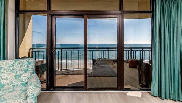 Een balkon met uitzicht op de oceaan, een schuifdeur en een gestreept bankje.