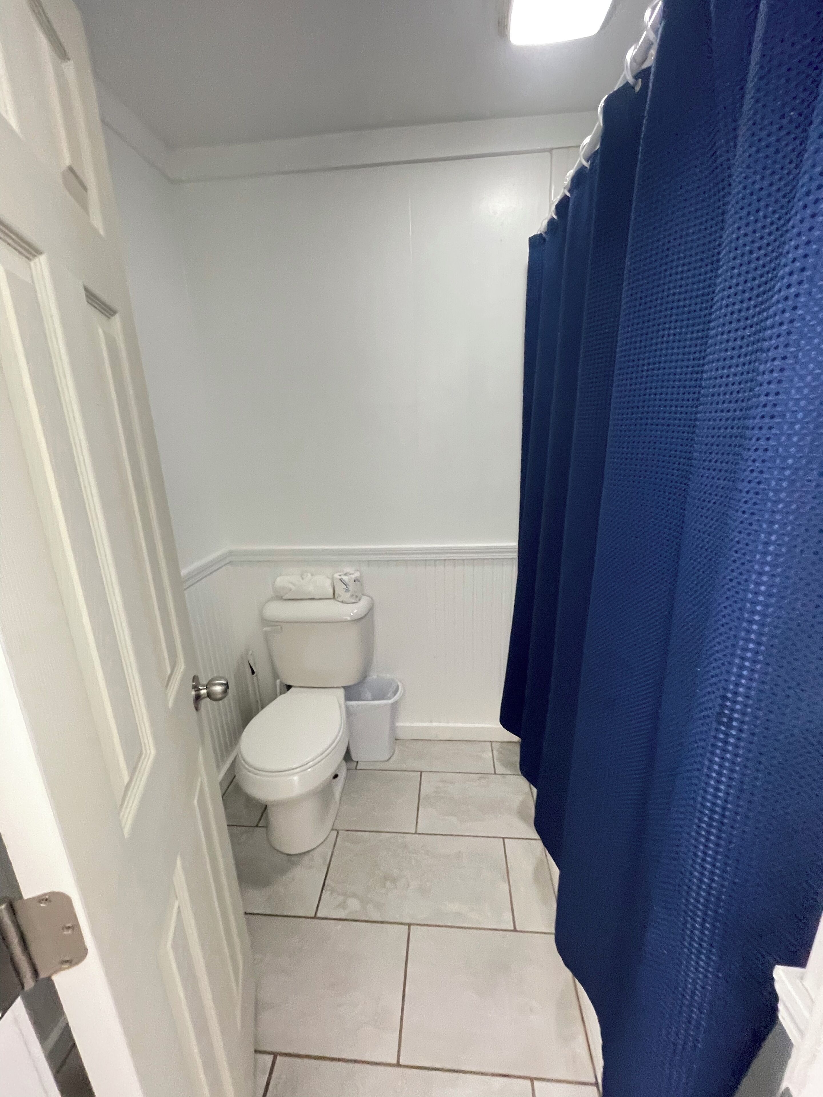 Une salle de bain avec des toilettes, une poubelle et un rideau de douche bleu.