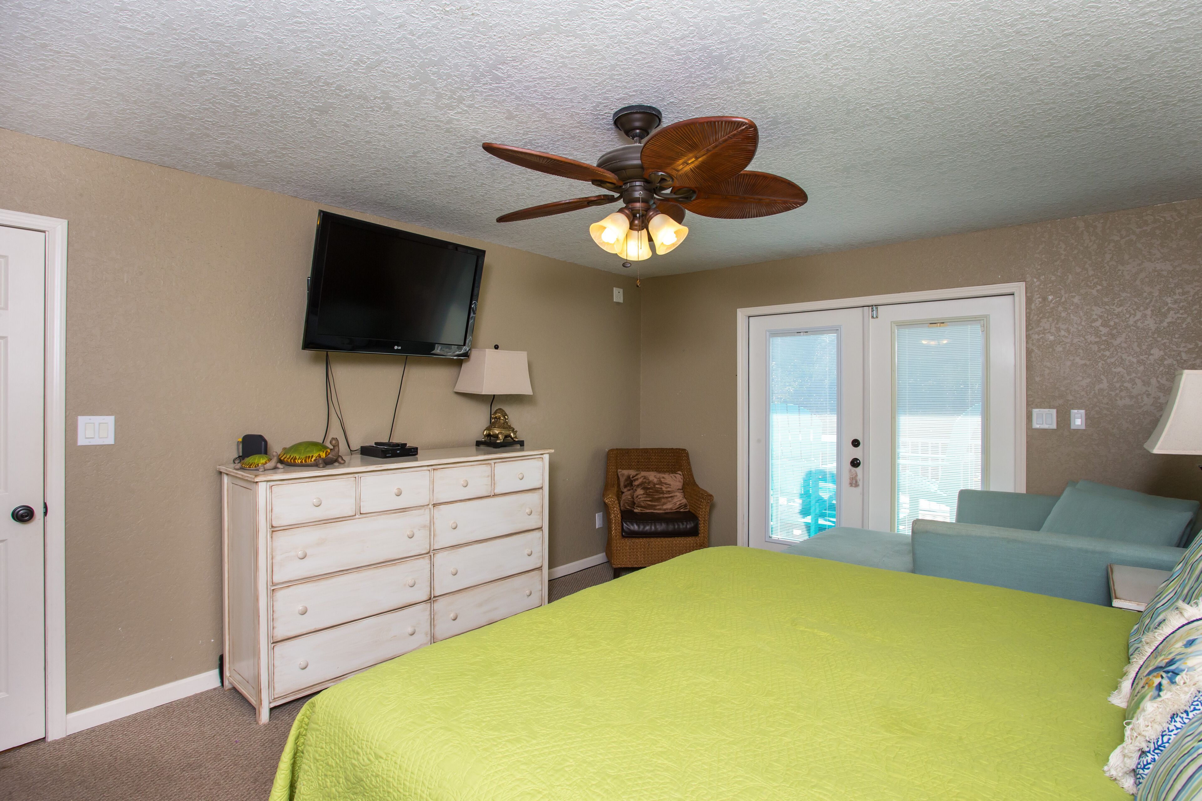 A bedroom with a bed, a dresser, a chair, a television, and a ceiling fan.