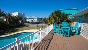 Une terrasse en bois avec une piscine, des fauteuils Adirondack turquoise et une clôture blanche.