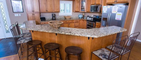 A kitchen with wooden cabinets, a granite countertop, a central island with stools, and stainless steel appliances.