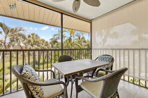 A balcony with wicker furniture, a table, and a view of palm trees.