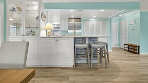 Una cocina moderna con una isla central, muebles blancos y una pared de acento color aguamarina.