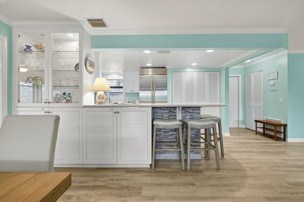 A modern kitchen with a central island, white cabinetry, and a teal accent wall.