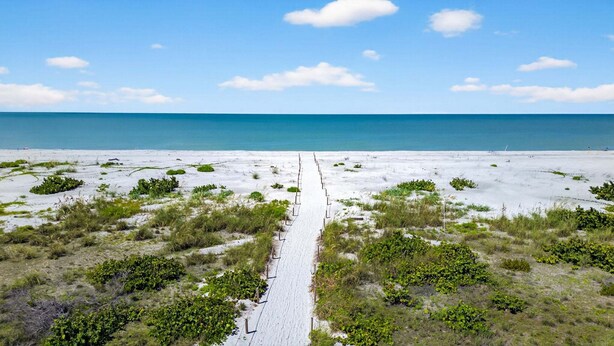 Una playa arenosa con un sendero estrecho que lleva al océano, rodeada de vegetación dispersa.