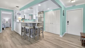 Una cocina con una isla central, taburetes de bar, un refrigerador y una mesa de comedor.