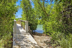 A wooden boardwalk leading to a small wooden structure near a body of water, surrounded by dense greenery.