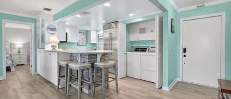 A modern kitchen with white cabinetry, a central island with bar stools, and a built-in oven.
