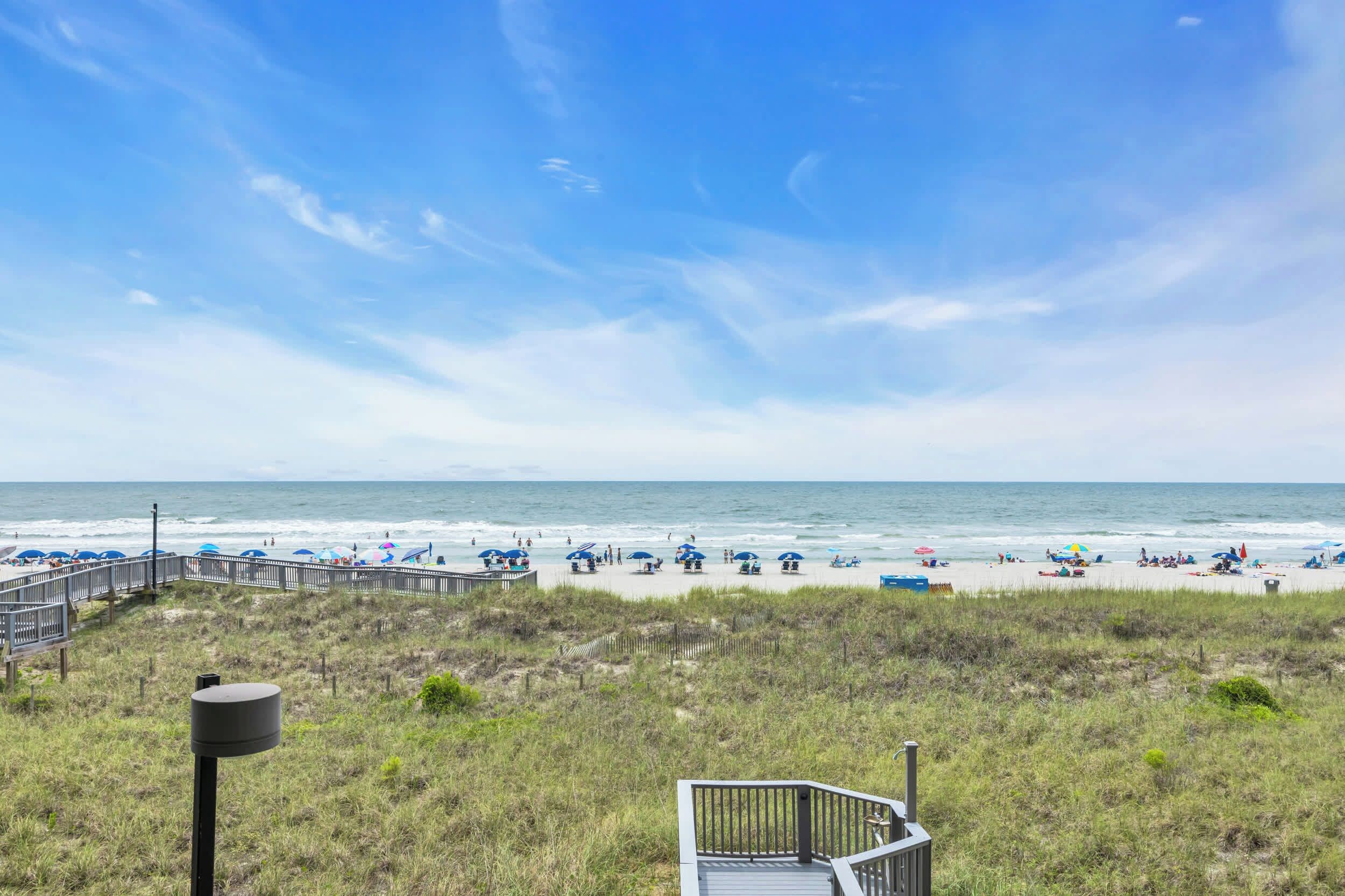 A beach with a wooden boardwalk leading to the shore, a grassy area in the foreground, and the ocean in the background.