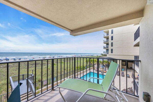 A balcony with a view of the beach and a pool.