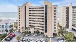 Ein mehrstöckiges Hotel mit Parkplatz vor der Tür, Blick auf den Strand und modernem architektonischen Design.