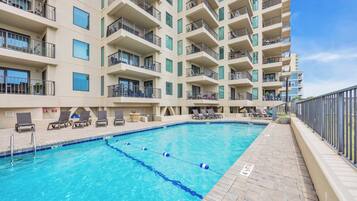 A swimming pool with lounge chairs and a building with multiple balconies.