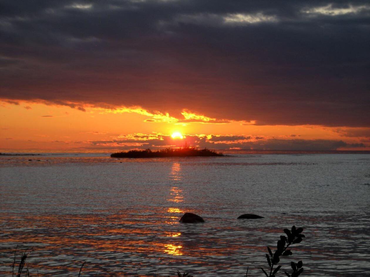 Un atardecer sobre un mar tranquilo con una isla a lo lejos.