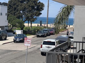 Une rue bordée de voitures garées, un panneau indiquant « INTERDICTION DE STATIONNER LE LUNDI DE 8 H À 12 H », une voiture blanche et une vue sur l’océan.