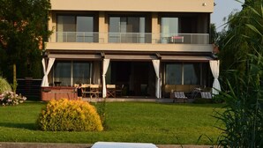 Una casa moderna de dos pisos con un porche cubierto y un muelle de madera que se adentra en el agua.