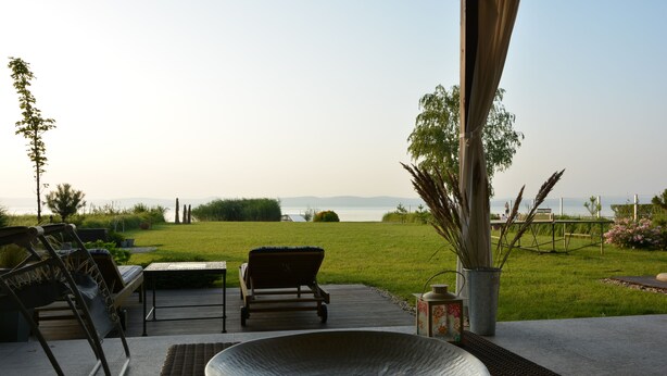 Un patio al aire libre con vista al mar, una silla de mimbre, una mesa y un cuenco decorativo.