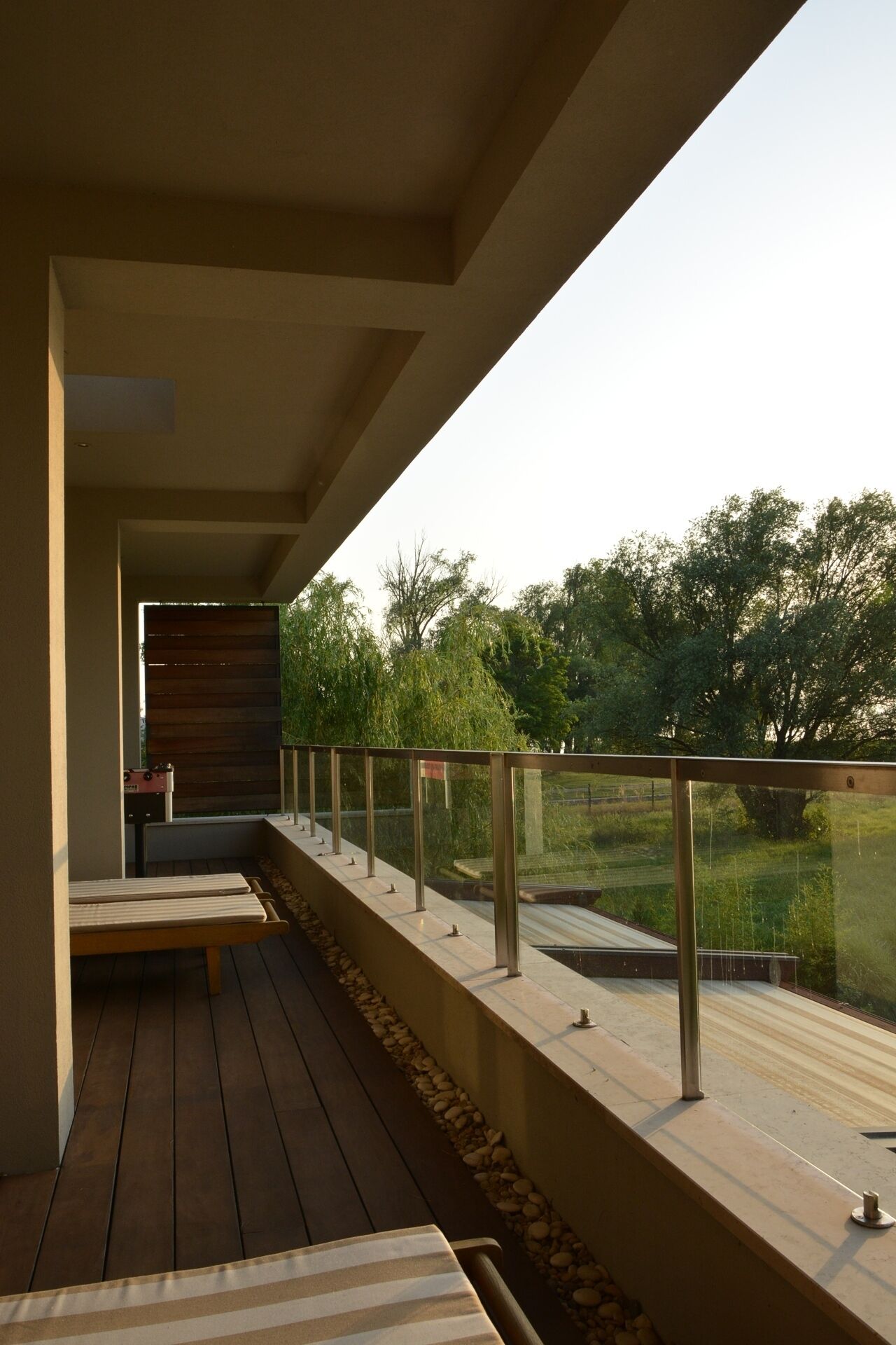 A modern outdoor deck with a wooden floor, a metal railing, and a view of a green landscape.