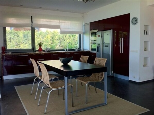 A modern kitchen with a dining table, chairs, and a refrigerator.