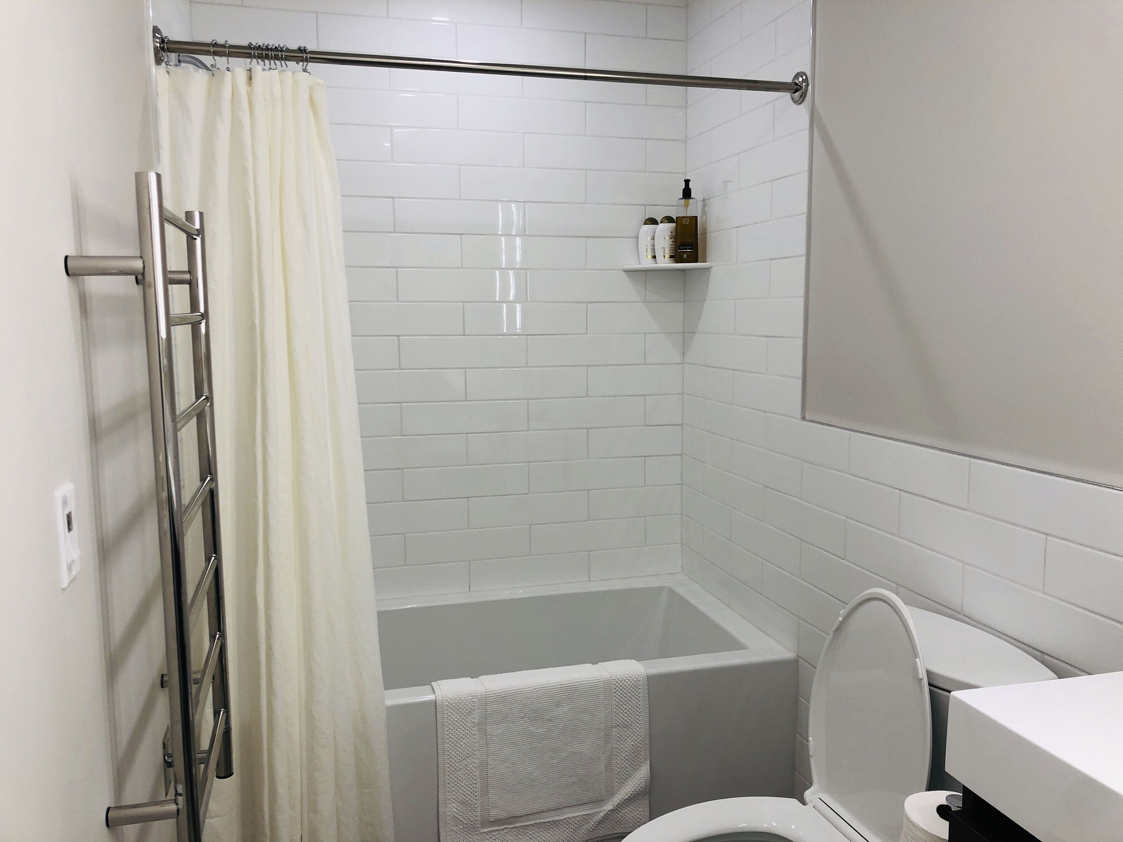 A bathroom with a shower, a bathtub, and a toilet. There is a towel rack and a shelf with toiletries.