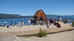 A wooden pier leading to a dock with a cabin, surrounded by boats and people on a sunny day.