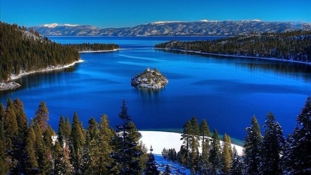A large body of water surrounded by dense forests and snow-covered mountains.