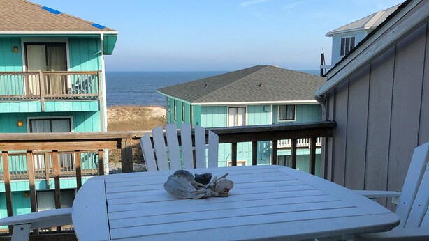 A white picnic table with chairs on a balcony overlooking the ocean, with turquoise buildings in the background.