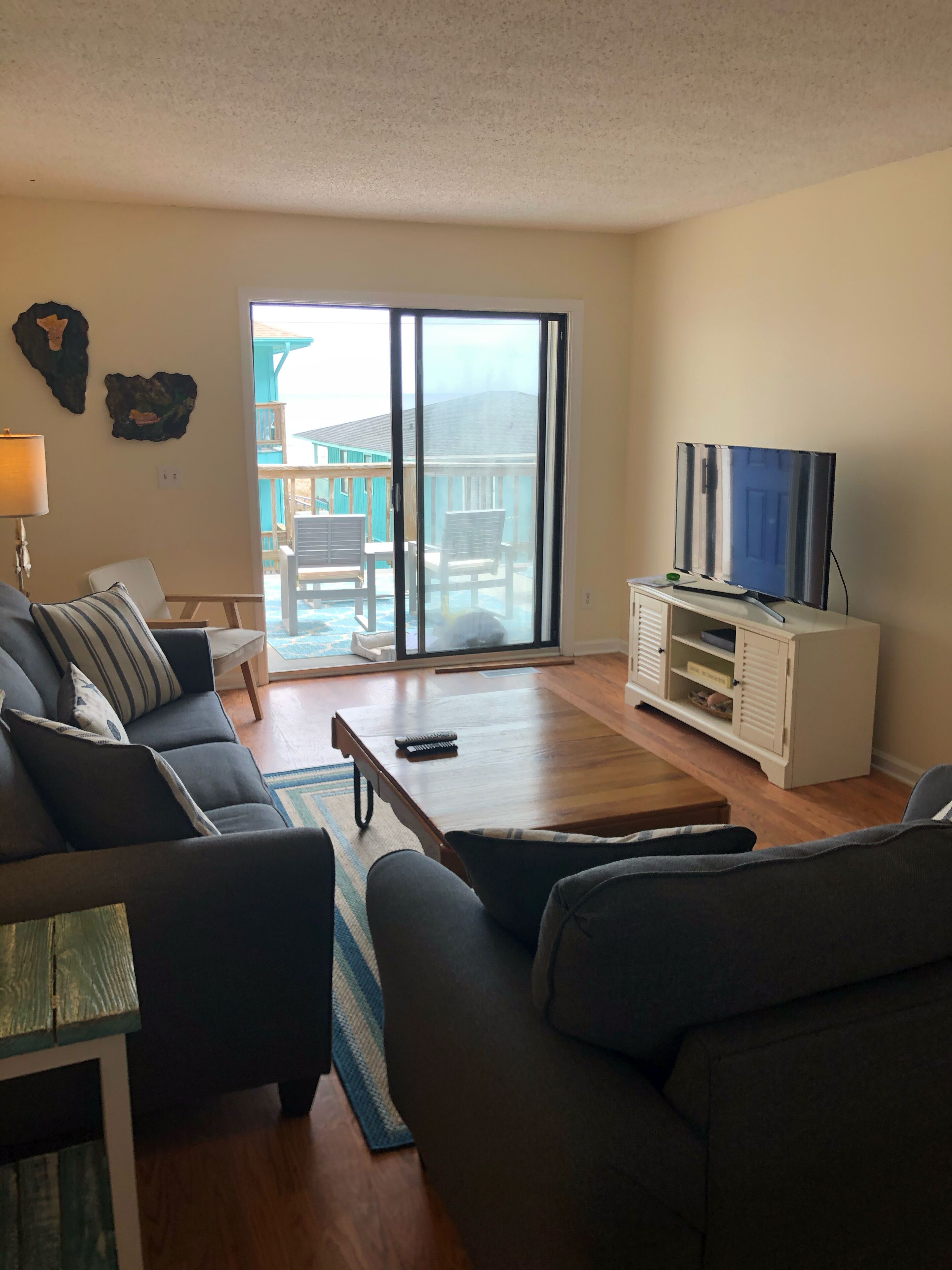 A living room with a sofa, a coffee table, a TV on a stand, and a sliding glass door leading to an outdoor area with a deck.