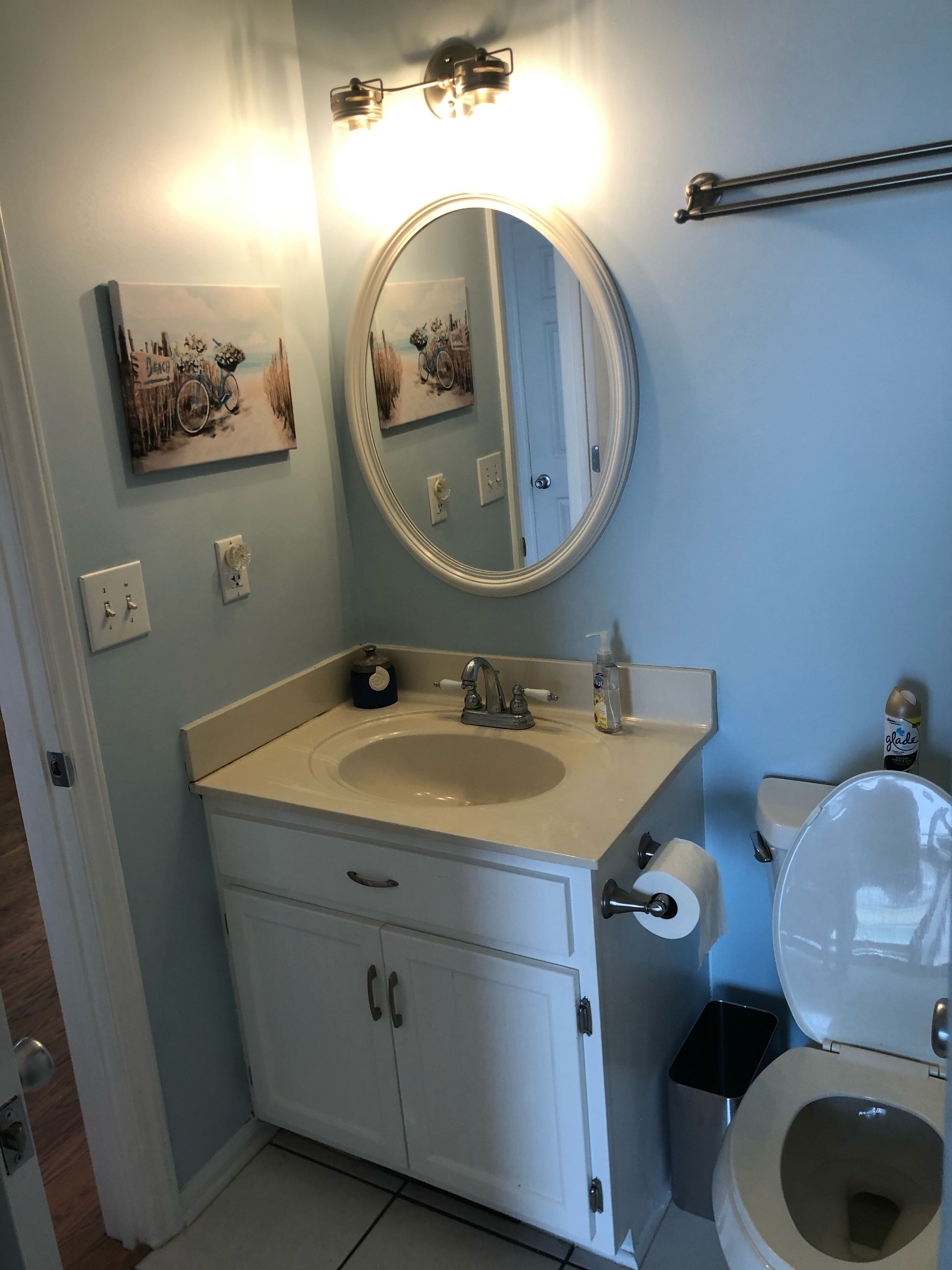 Une salle de bain équipée d’un lavabo, d’un miroir, de toilettes et d’une poubelle.