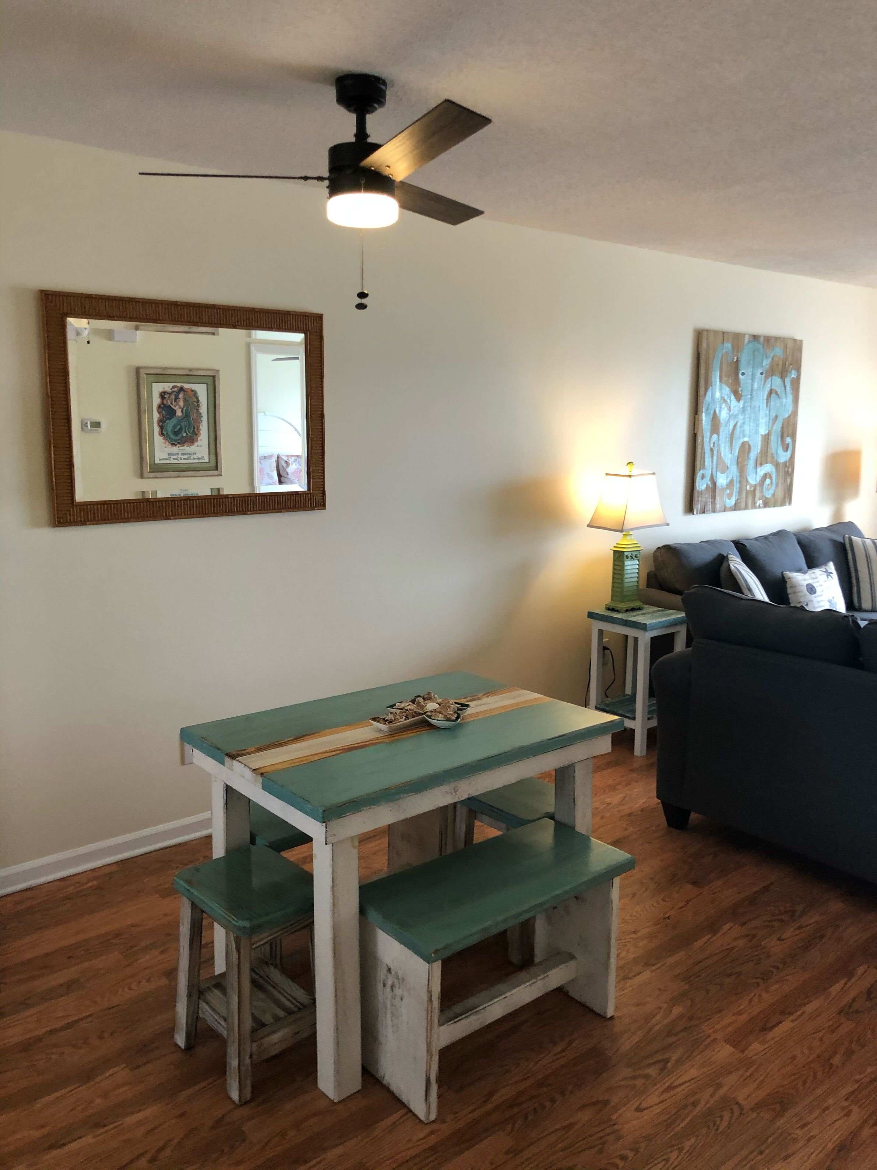 A dining area with a wooden table and benches, a ceiling fan, a lamp, and a couch.