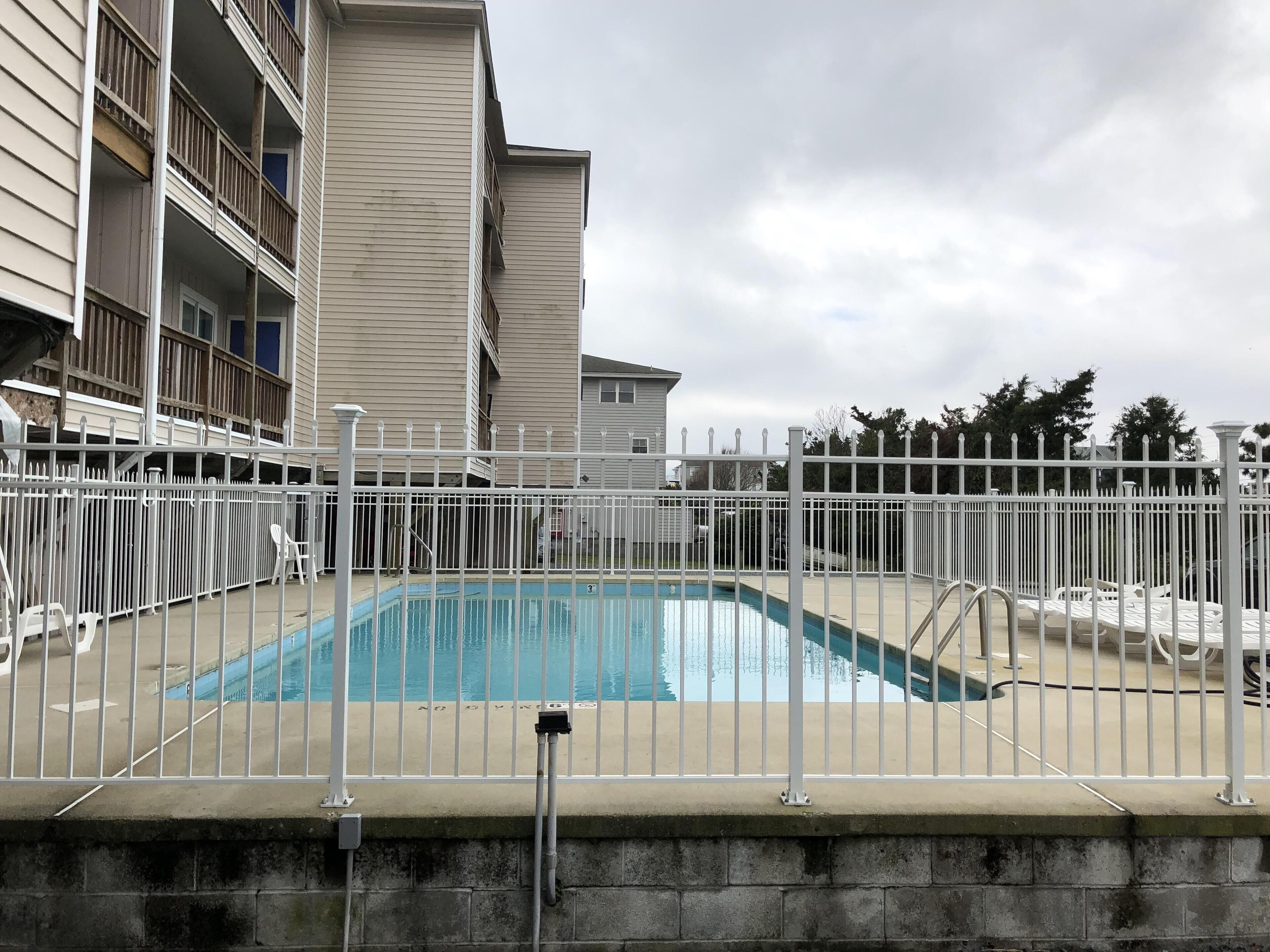 Piscina cercada por uma cerca branca, com um edifício ao fundo.
