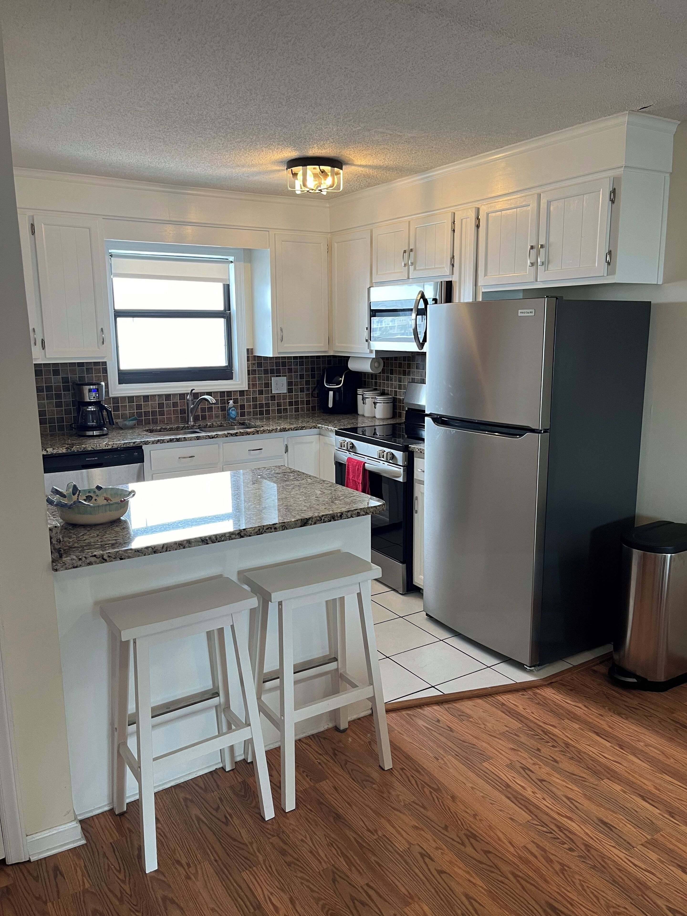 A modern kitchen with white cabinets, a stainless steel refrigerator, a microwave, and a coffee maker.