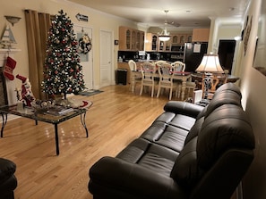A living room with a black leather sofa, a glass coffee table, and a Christmas tree.
