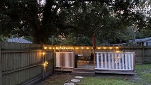 Un patio trasero con valla de madera, terraza y guirnalda de luces.
