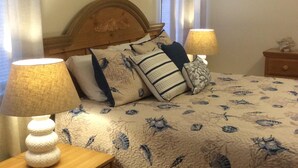 Un dormitorio con una cama, dos mesitas de noche, una mesilla auxiliar, un cabecero de madera y una obra de arte en la pared.