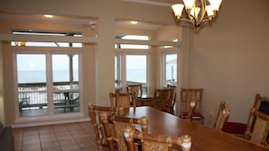 Un comedor espacioso con una gran mesa de madera y sillas, ventanas amplias con vista al océano y un candelabro.