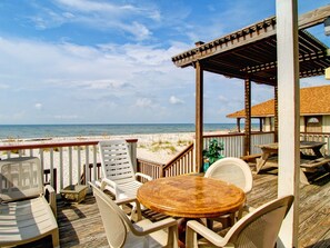 Una terraza de madera con mobiliario exterior, incluyendo sillas y una mesa, con vistas a la playa.
