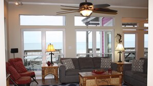 Amplia sala de estar con un gran ventanal con vistas al mar, un ventilador de techo y una mesa de centro de madera.