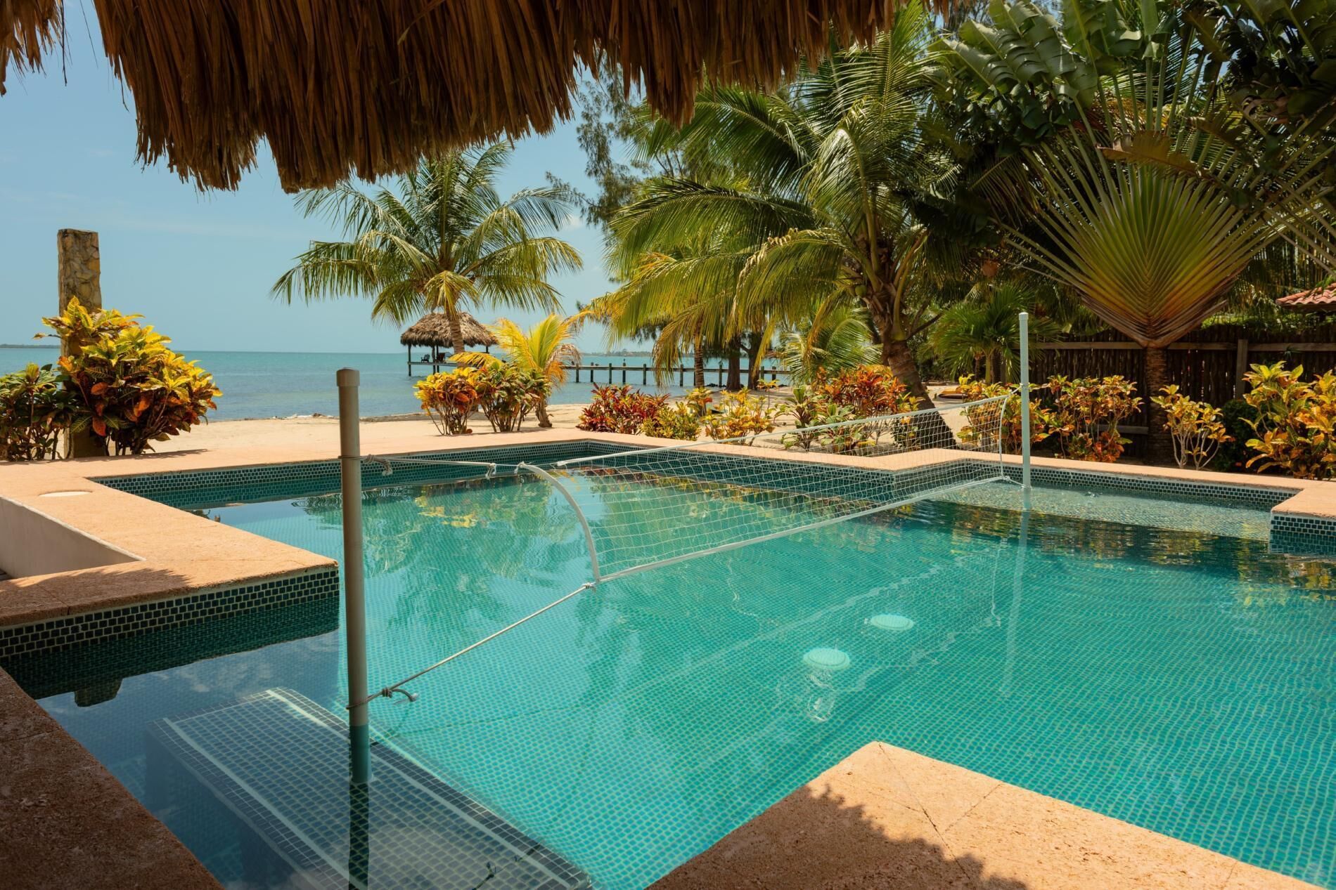 Una piscina con agua azul cristalina, rodeada de plantas tropicales y palmeras, con vista al mar.