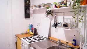 Une cuisine de taille réduite, équipée d’une cuisinière à gaz, d’un évier et d’étagères où sont rangés divers ustensiles de cuisine.