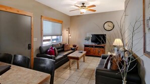 A living room with a sofa, coffee table, TV stand, and a ceiling fan. - Arrowhead Properties Unit 4 (West Yellowstone)
