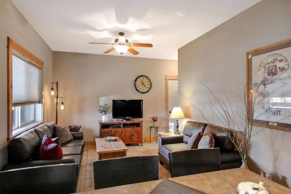 A living room with a sofa set, a TV, a wooden coffee table, and a ceiling fan.