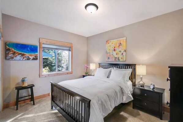 A bedroom with a bed, a nightstand, a dresser, a window with a view, and two paintings on the wall.