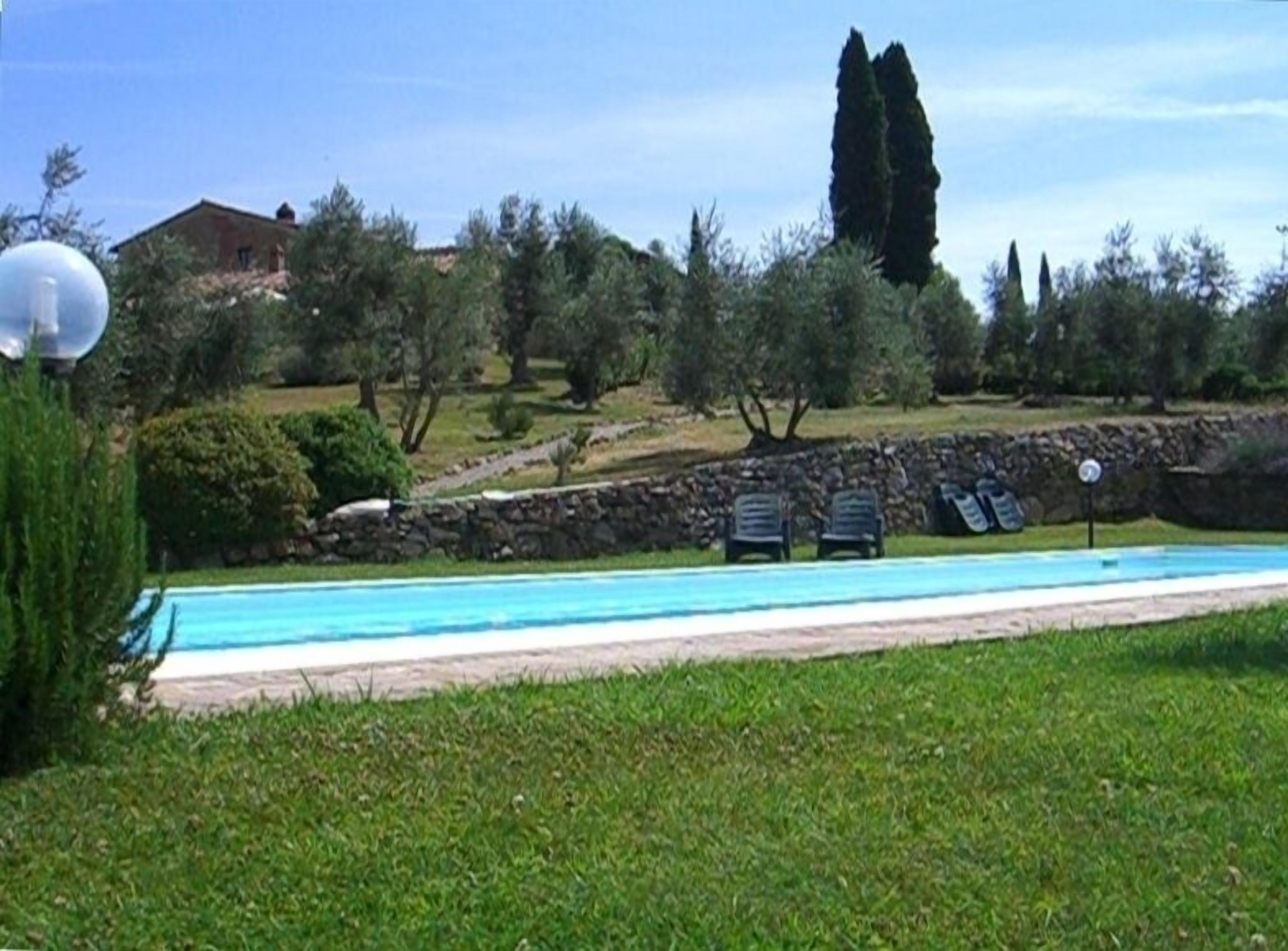 A swimming pool with a stone wall and a grassy area.